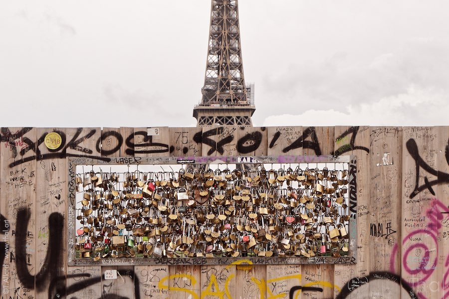 Opening in a palisade covered with padlocks in front of the Eiffel Tower